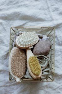 Top view of natural spa tools in a wire basket on a white fabric surface.