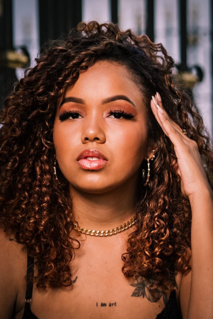 Close-up portrait of a woman with curly hair and chain necklace, exuding confidence and elegance.