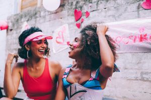 Two women laughing together at a colorful outdoor celebration with heart decorations.