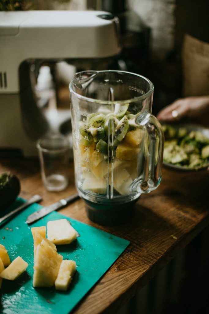 Close-up of a blender with kiwi and pineapple chunks ready to make a smoothie in a cozy kitchen setting.