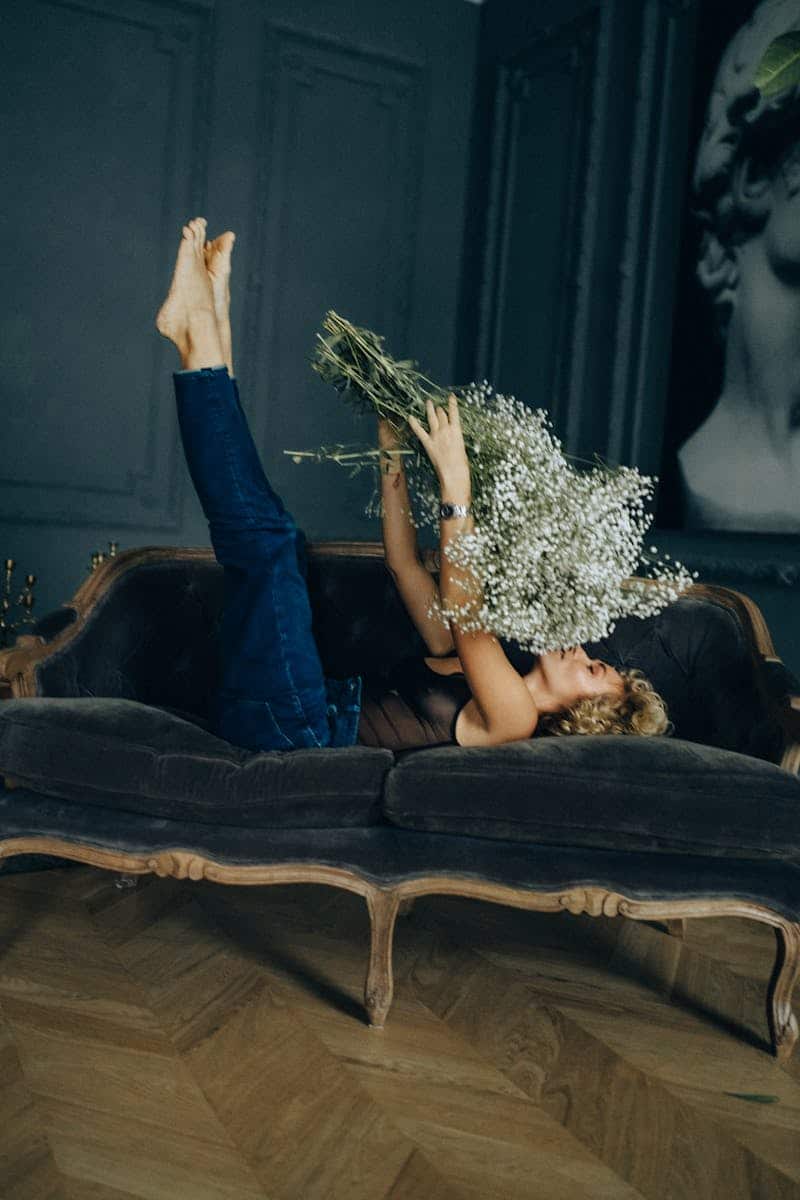 A woman lounging on a vintage sofa holding white flowers, creating a relaxing home vibe.