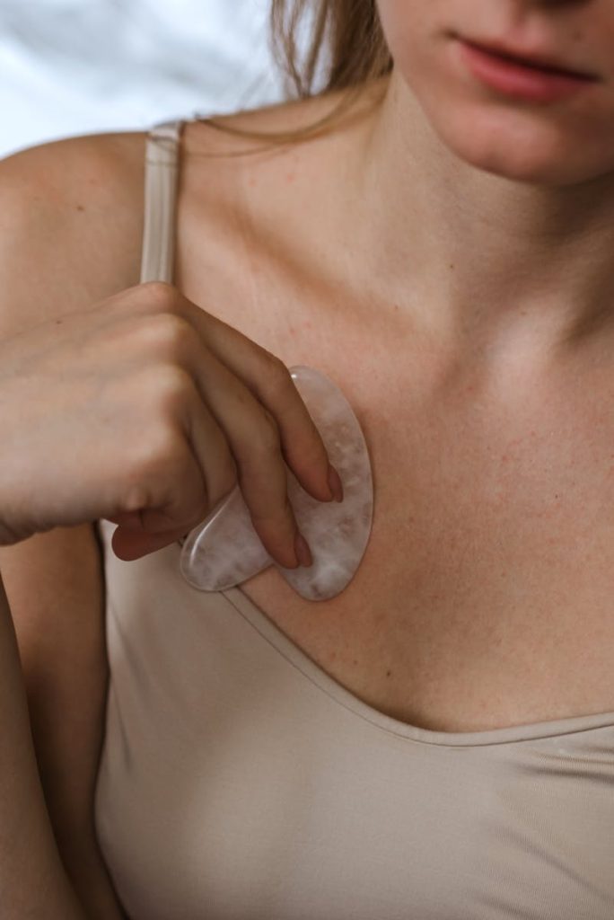 Close-up of woman using a gua sha tool on her chest focusing on skincare and self-care.