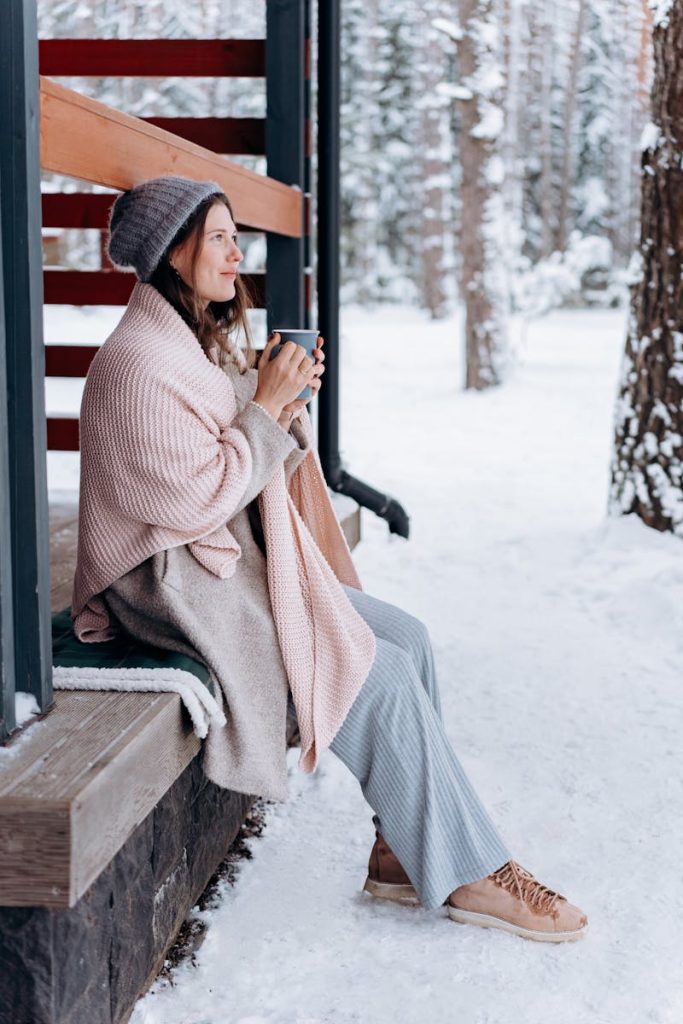 Woman enjoying a hot drink outside in a cozy winter setting, wrapped in warm clothes.